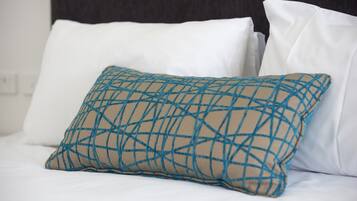 A bed with white linens and a single decorative pillow with a geometric pattern.