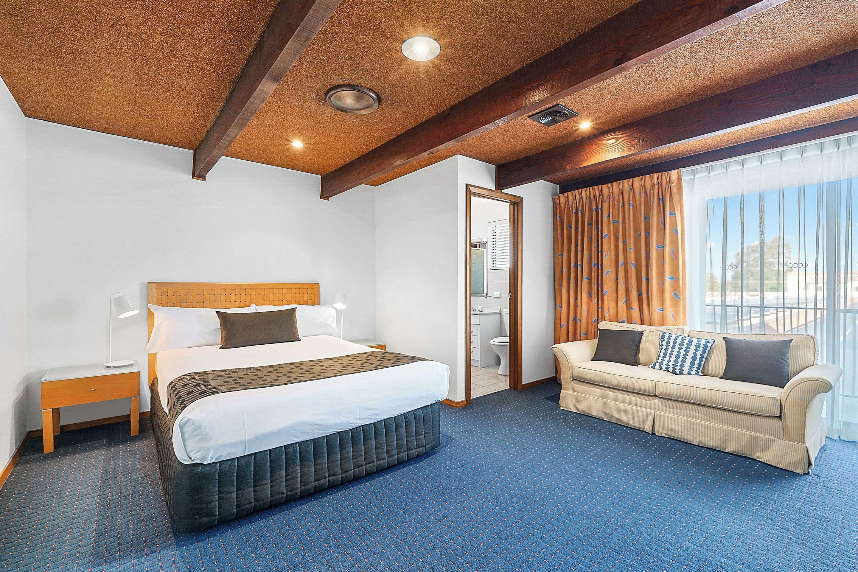 A hotel room with a bed, a sofa, a nightstand, and a bathroom visible through an open door.