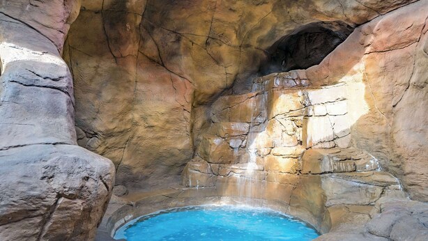 A natural hot spring with clear water, surrounded by rocky formations and a waterfall.