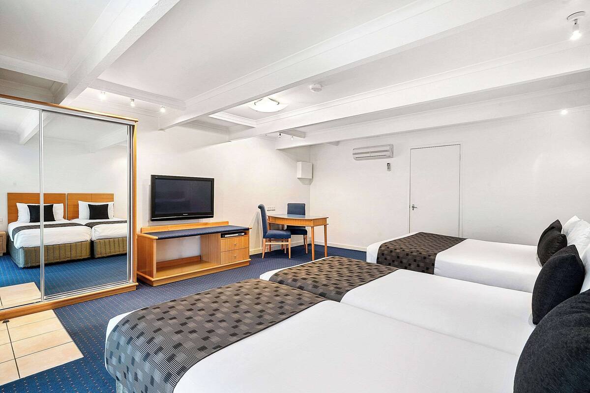 A hotel room with two beds, a desk with a chair, a television, and a wardrobe.