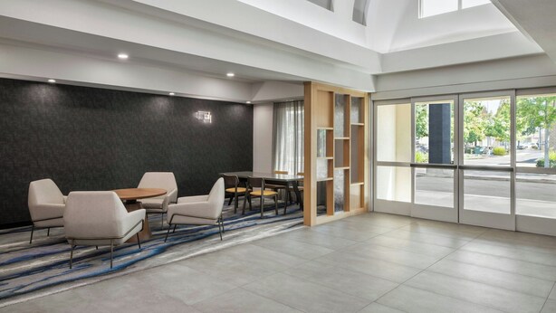 Una habitación de hotel moderna con un ventanal grande, un área de comedor con una mesa redonda y sillas, y una pared de acento oscura.