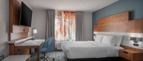 A hotel room with a bed, desk, chair, TV, and a window with curtains.