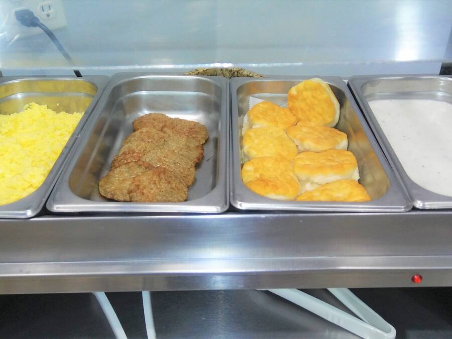 A buffet with trays of food including mashed potatoes, fried meat, biscuits, and a white sauce.