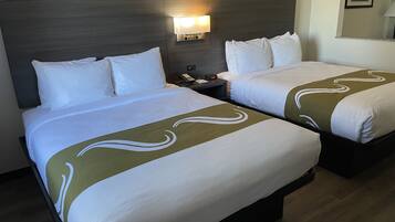Quarto de hotel com duas camas, cada uma com roupa de cama branca e detalhes verdes. Há uma mesa de cabeceira com telefone e abajur entre as camas.