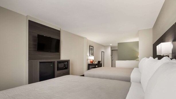 Habitación de hotel con dos camas, un televisor de pantalla plana, un microondas y un escritorio con lámpara.