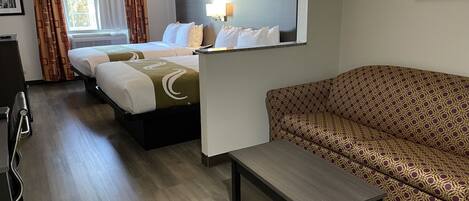 Ein Hotelzimmer mit zwei Betten, einer Couch, einem kleinen Tisch und einem Spiegel.