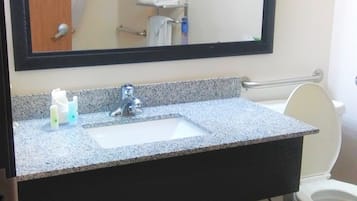 A bathroom with a granite countertop, a sink, a mirror, a toilet, and a shower area.