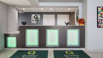 A hotel reception area with a modern design, featuring a reception desk with illuminated panels, a digital display, and a logo sign.