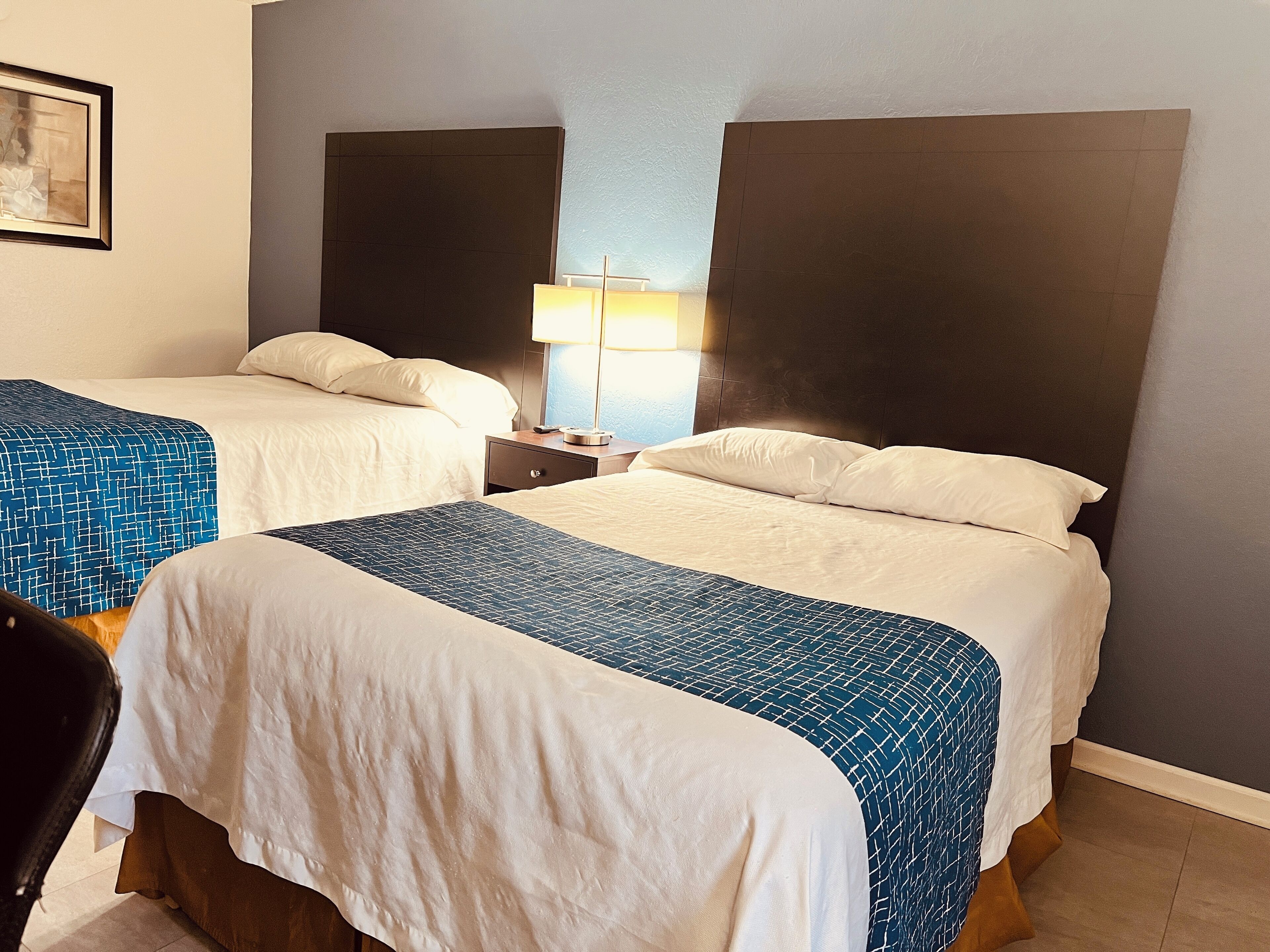 Habitación de hotel con dos camas, una mesita de noche con lámpara y un cuadro en la pared.