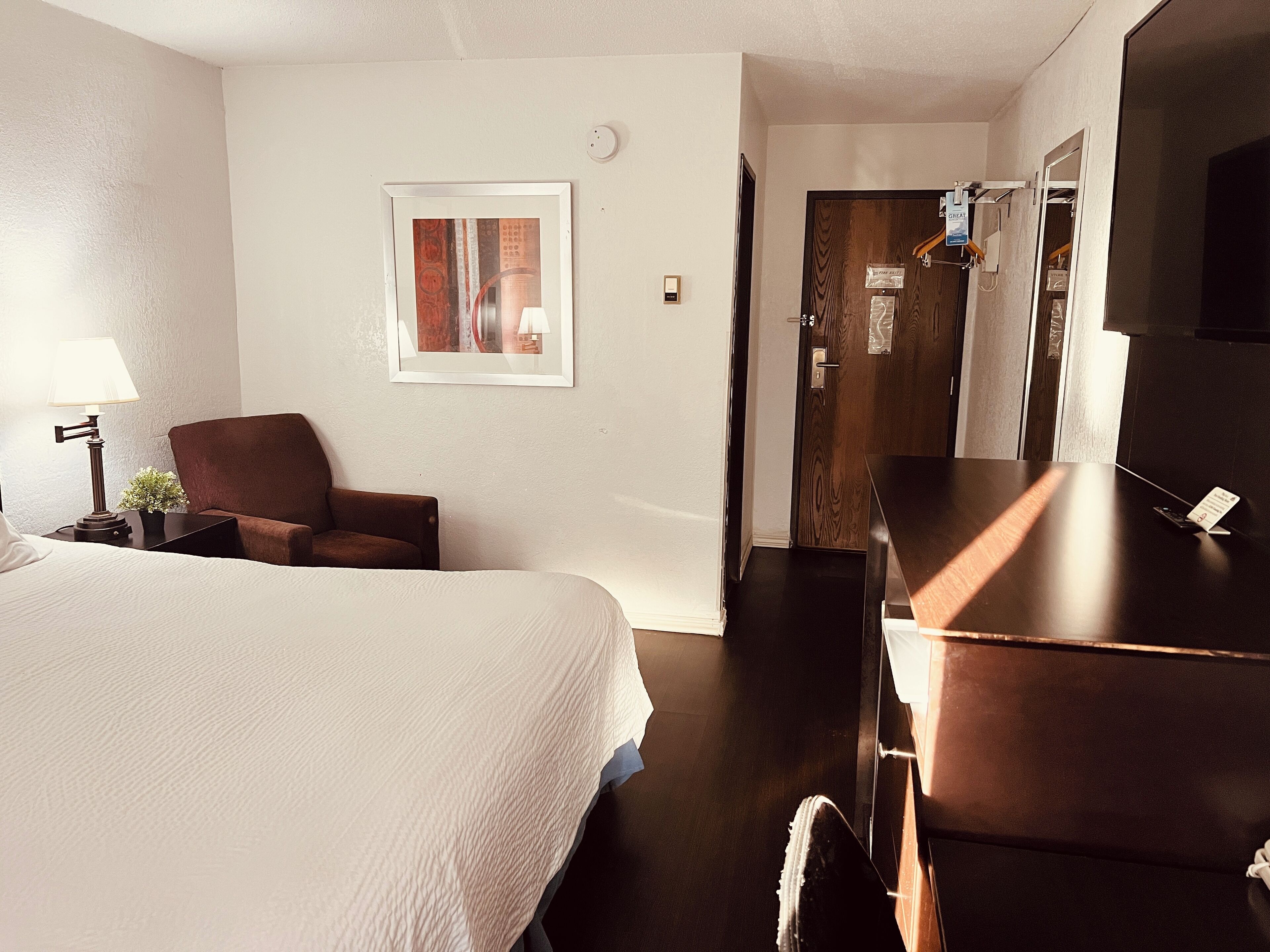 A hotel room with a bed, a chair, a desk, a lamp, and a framed picture on the wall.
