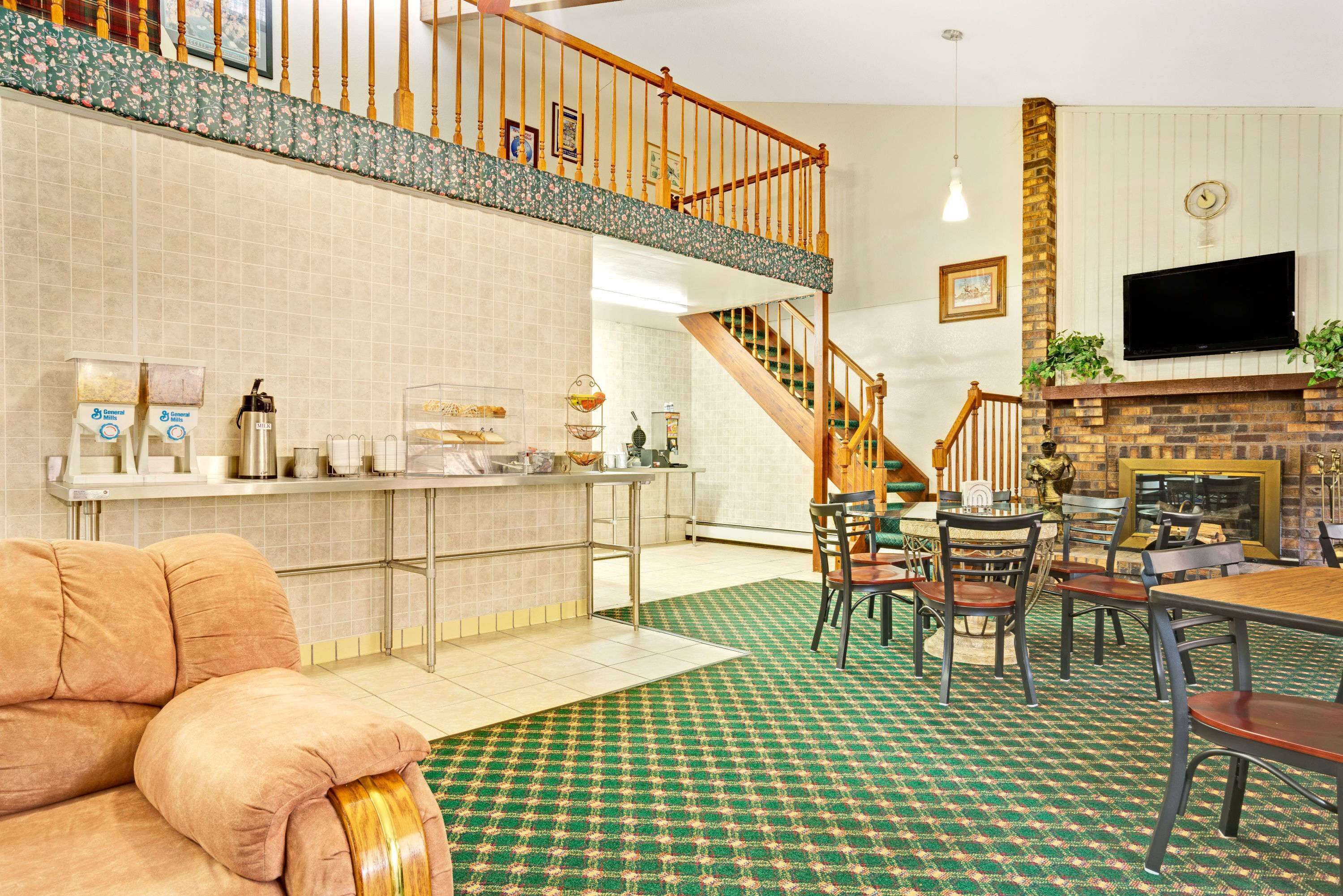 A spacious living area with a high ceiling, a kitchen area with a countertop and appliances, a staircase leading to an upper level, and a fireplace with a TV mounted above it.