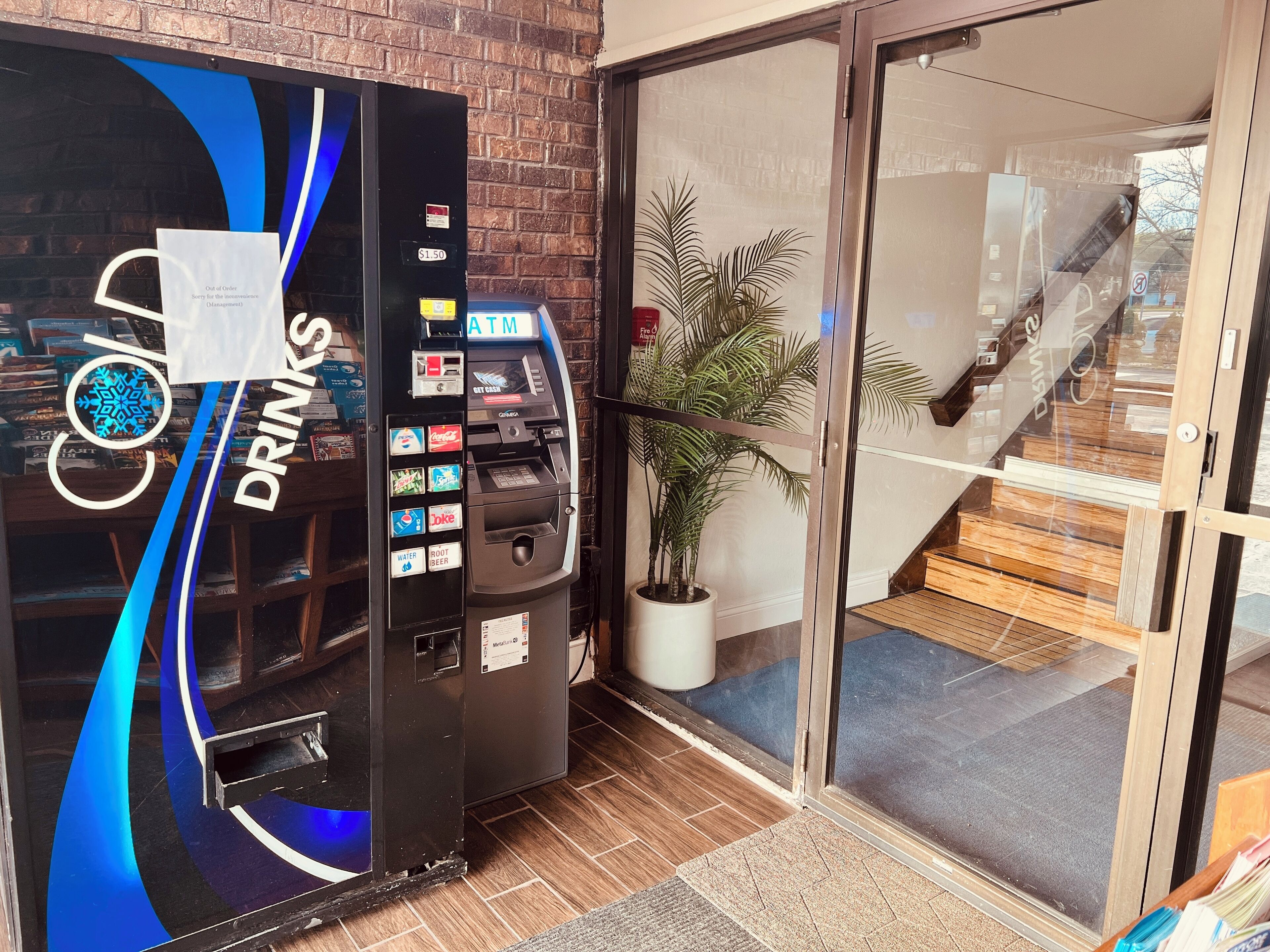 Un distributeur automatique portant l’inscription « Boissons », proposant une variété de boissons, une plante en pot et un escalier menant à un niveau supérieur.