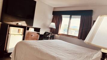 A hotel room with a bed, a desk with a computer, a microwave, and a television.