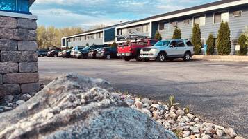 A parking lot with several cars, a building with multiple windows, and a stone wall.