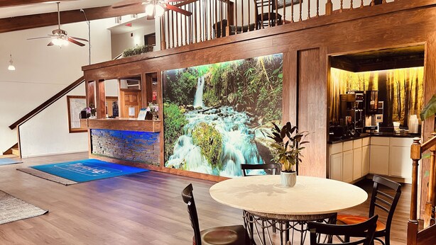 A modern kitchen with a waterfall mural, wooden flooring, and a round dining table with chairs. - Travelodge by Wyndham Valleyfair Shakopee (Shakopee)