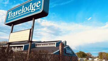 A Travelodge sign and building with a brick facade and a large lawn in front.