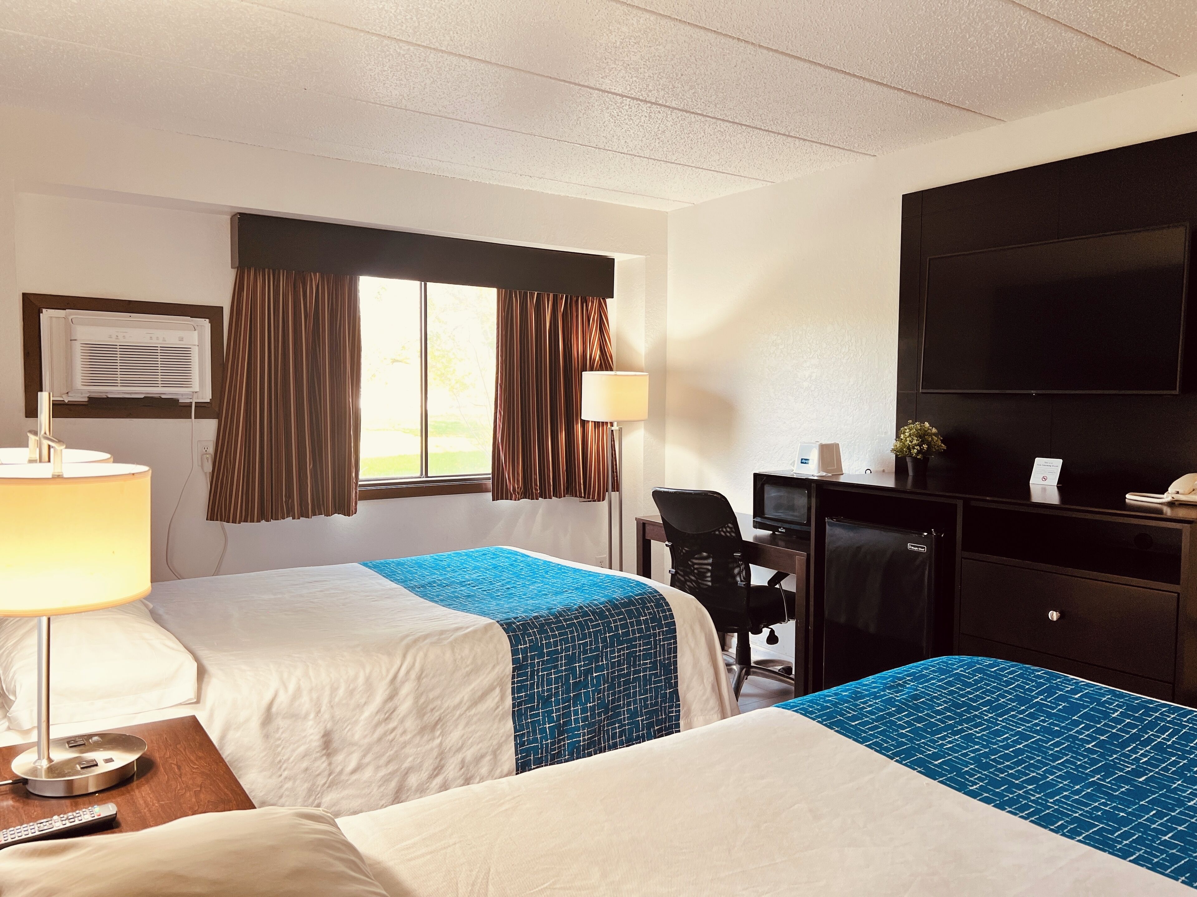 A hotel room with two beds, a desk, a TV, and a window with curtains.