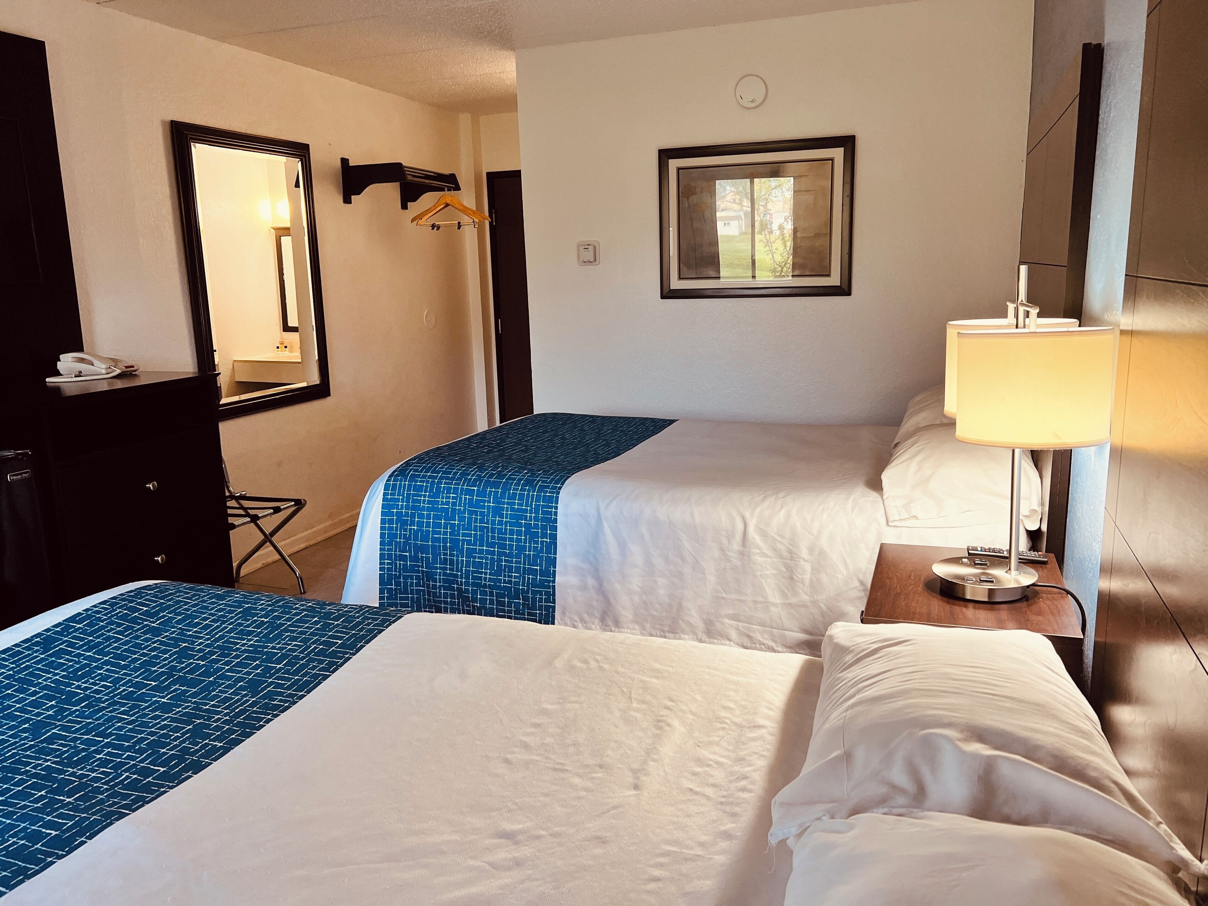 A hotel room with two beds, a desk, a mirror, a hanging coat rack, and a window with a view.