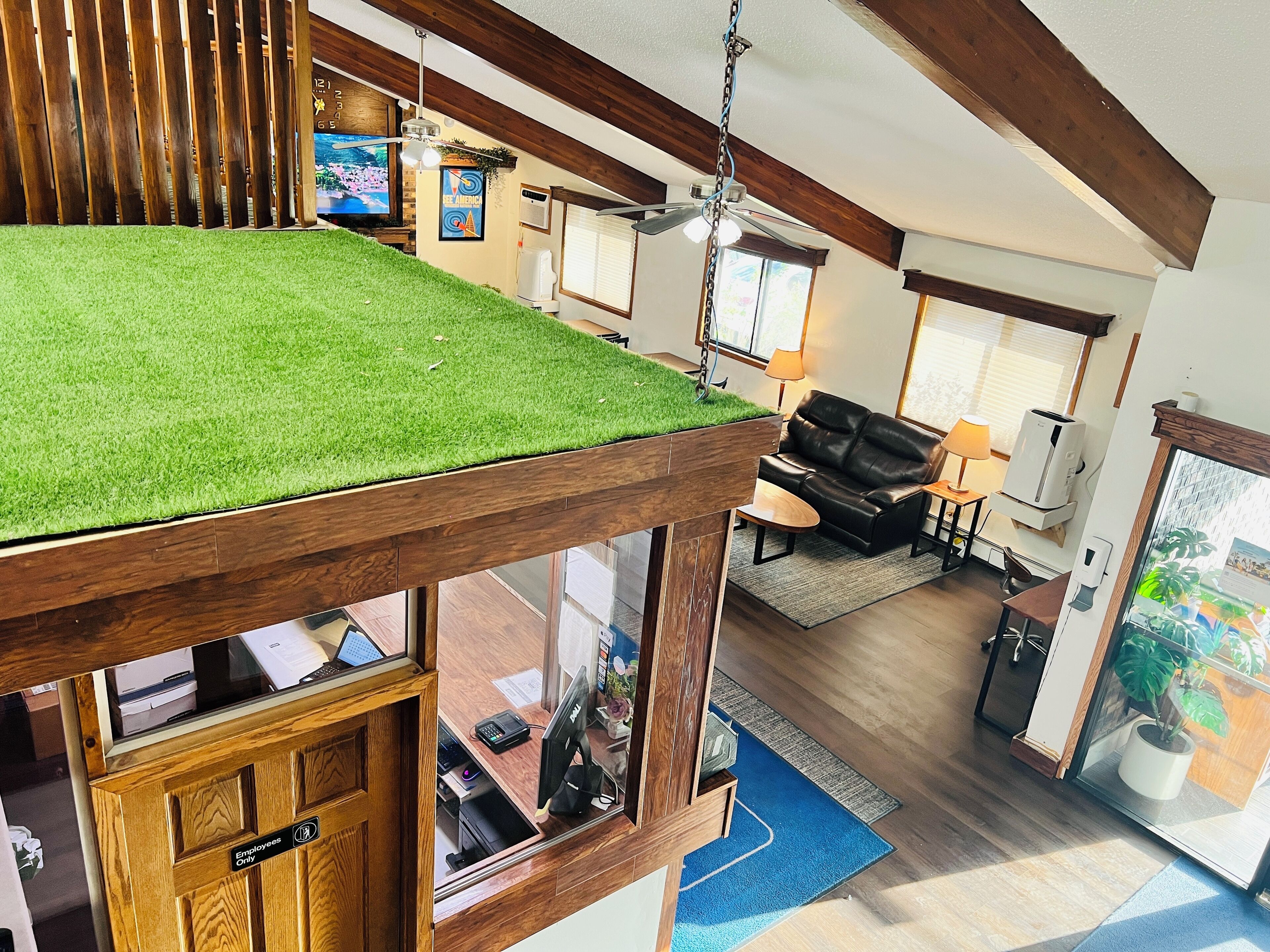 Un intérieur moderne avec un plafond en bois, un espace recouvert de gazon synthétique vert, un canapé en cuir et un bureau avec un ordinateur.