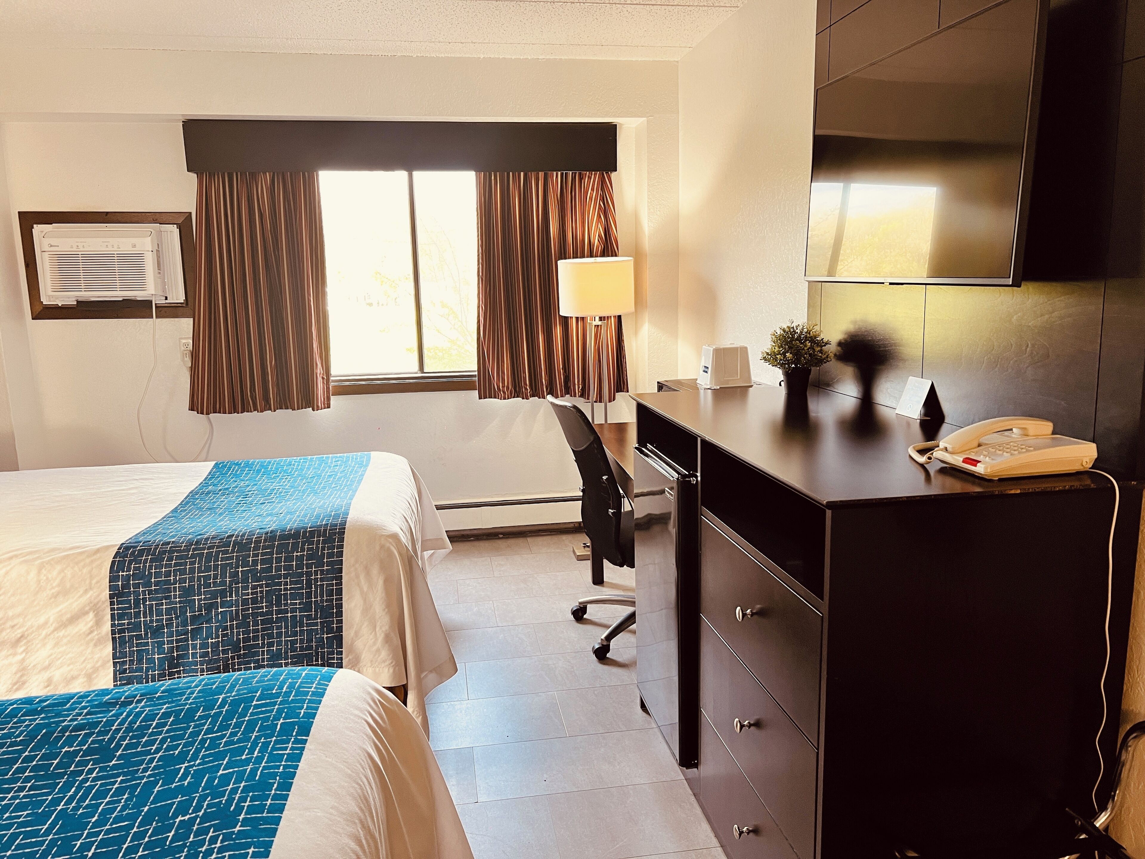 Quarto de hotel com duas camas, uma escrivaninha, um telefone e uma televis ão.