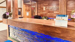 A wooden reception desk with a stone accent wall, a sign reading "Travelod by Wyndham", and a brochure on the counter. - Travelodge by Wyndham Valleyfair Shakopee (Shakopee)