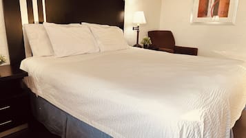 Un lit bien fait, avec du linge de lit blanc, une tête de lit sombre, une table de chevet avec une lampe et une petite plante en pot.
