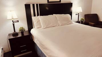 A neatly made bed with white linens and a black headboard, flanked by two bedside tables with lamps and small potted plants.