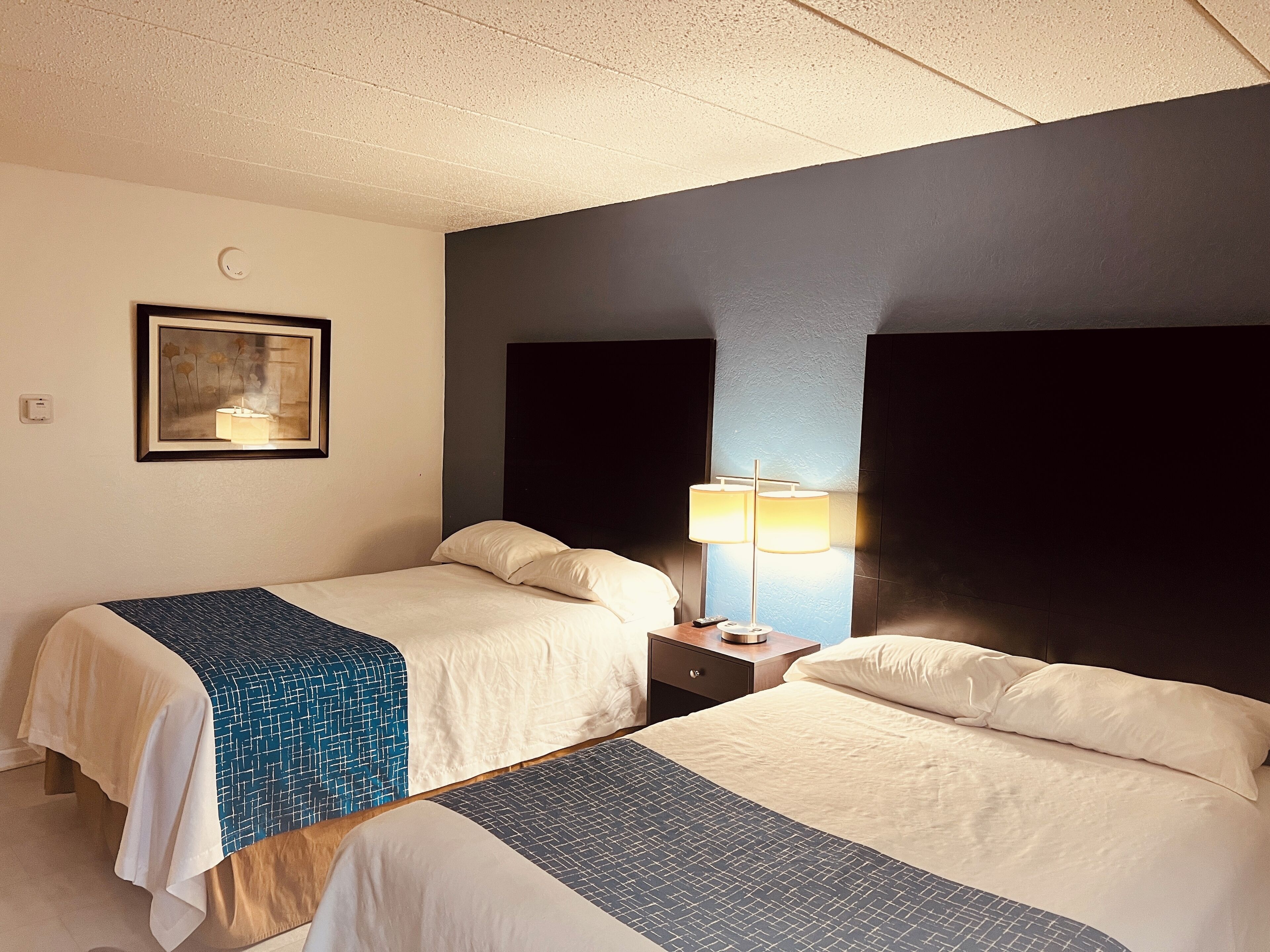 A hotel room with two beds, a nightstand with a lamp, a framed picture on the wall, and a ceiling with a textured finish.