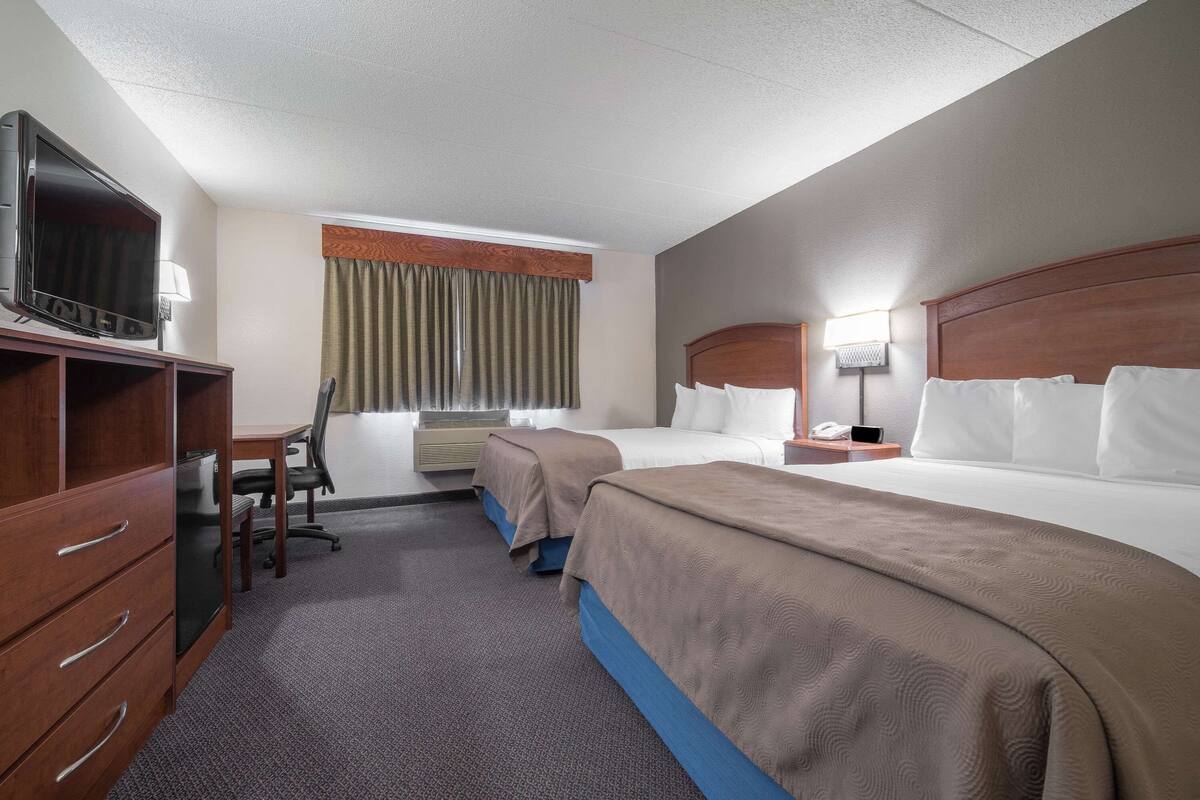 Habitación de hotel con dos camas, un escritorio con silla, televisor y ventana con cortinas.