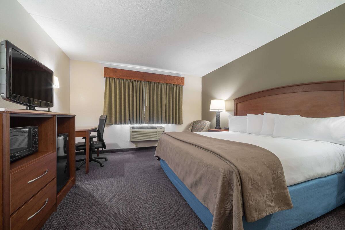 Habitación de hotel con cama, escritorio con televisor, silla, aire acondicionado y lámpara.