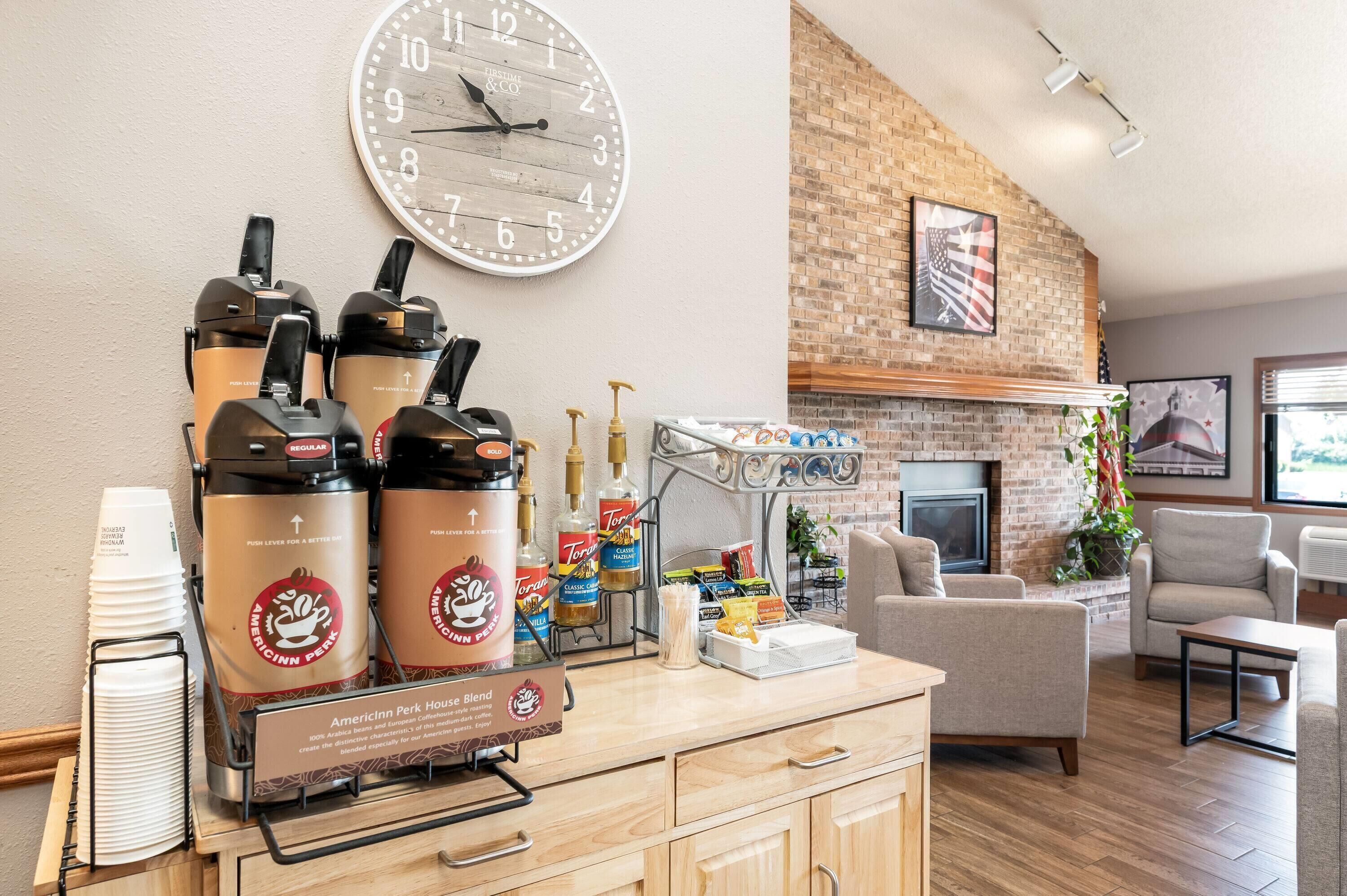 A coffee station with espresso machines, a clock, and a fireplace in a lounge area.