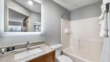 A bathroom with a granite countertop sink, a mirror, a toilet, and a bathtub.