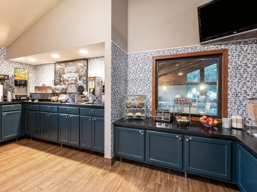 A kitchen with dark blue cabinets, a black countertop, a coffee machine, and a window with a view of trees.