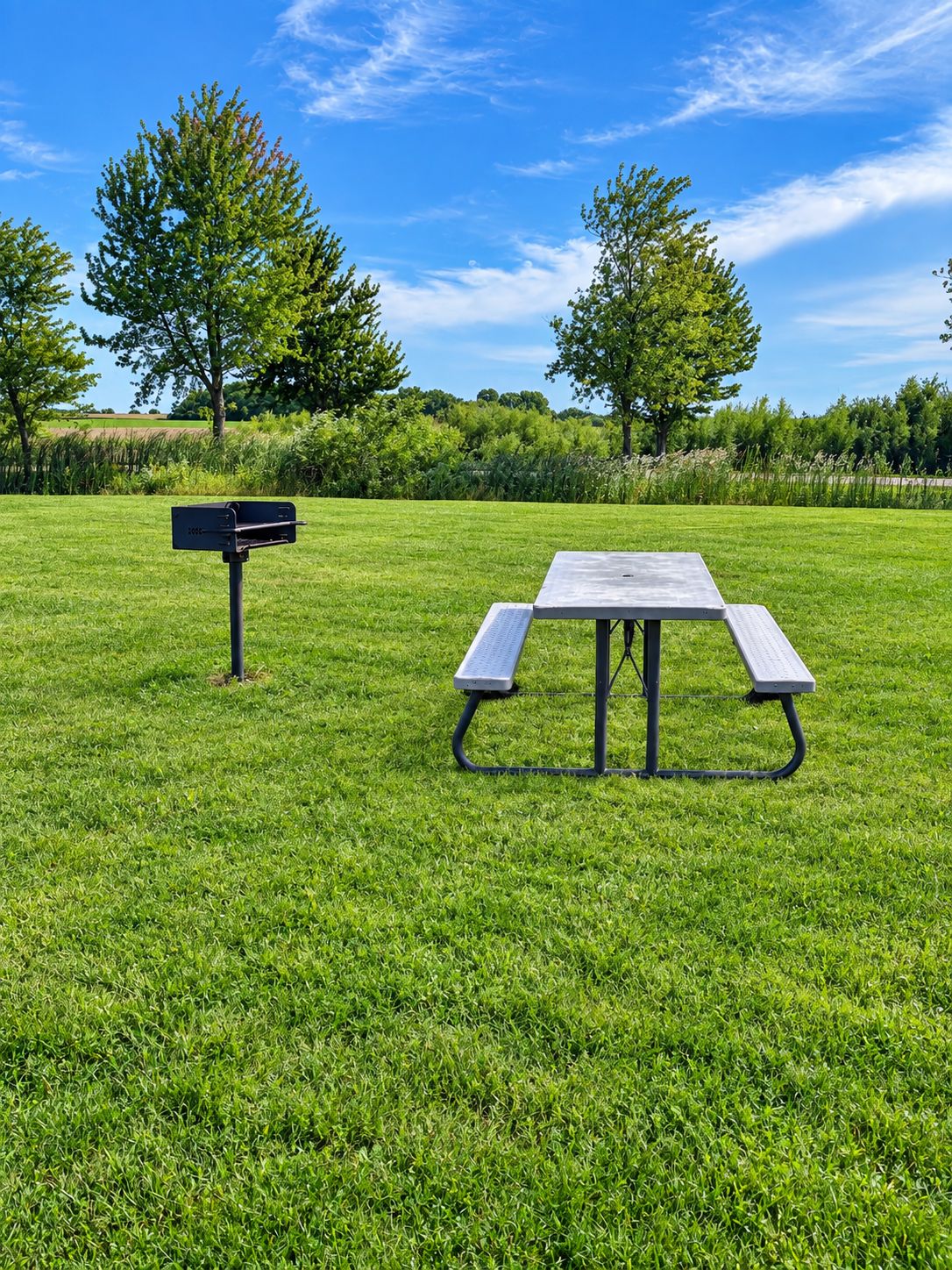 A picnic table with benches in a grassy field with trees in the background.