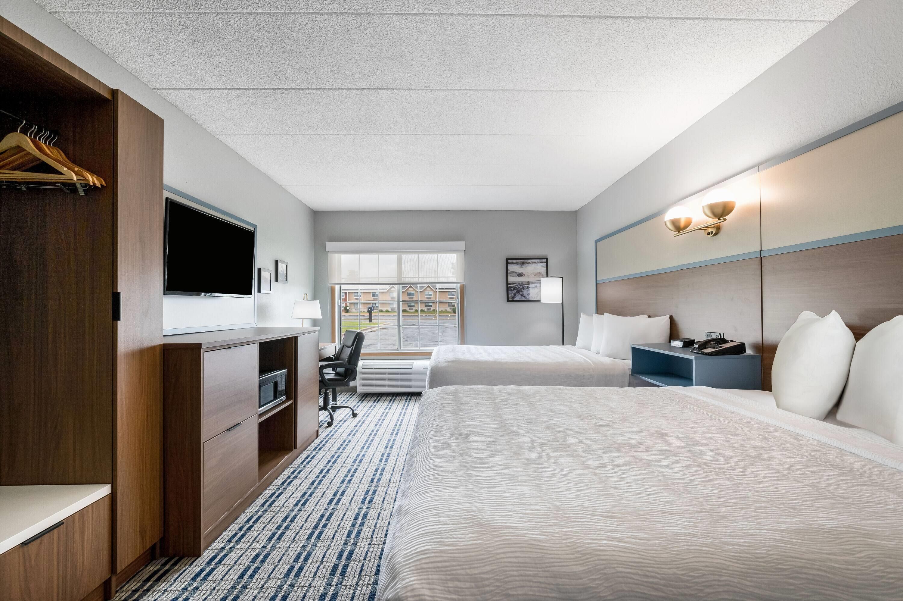 Habitación de hotel con cama, escritorio, silla, televisión y ventana con vistas a edificios.