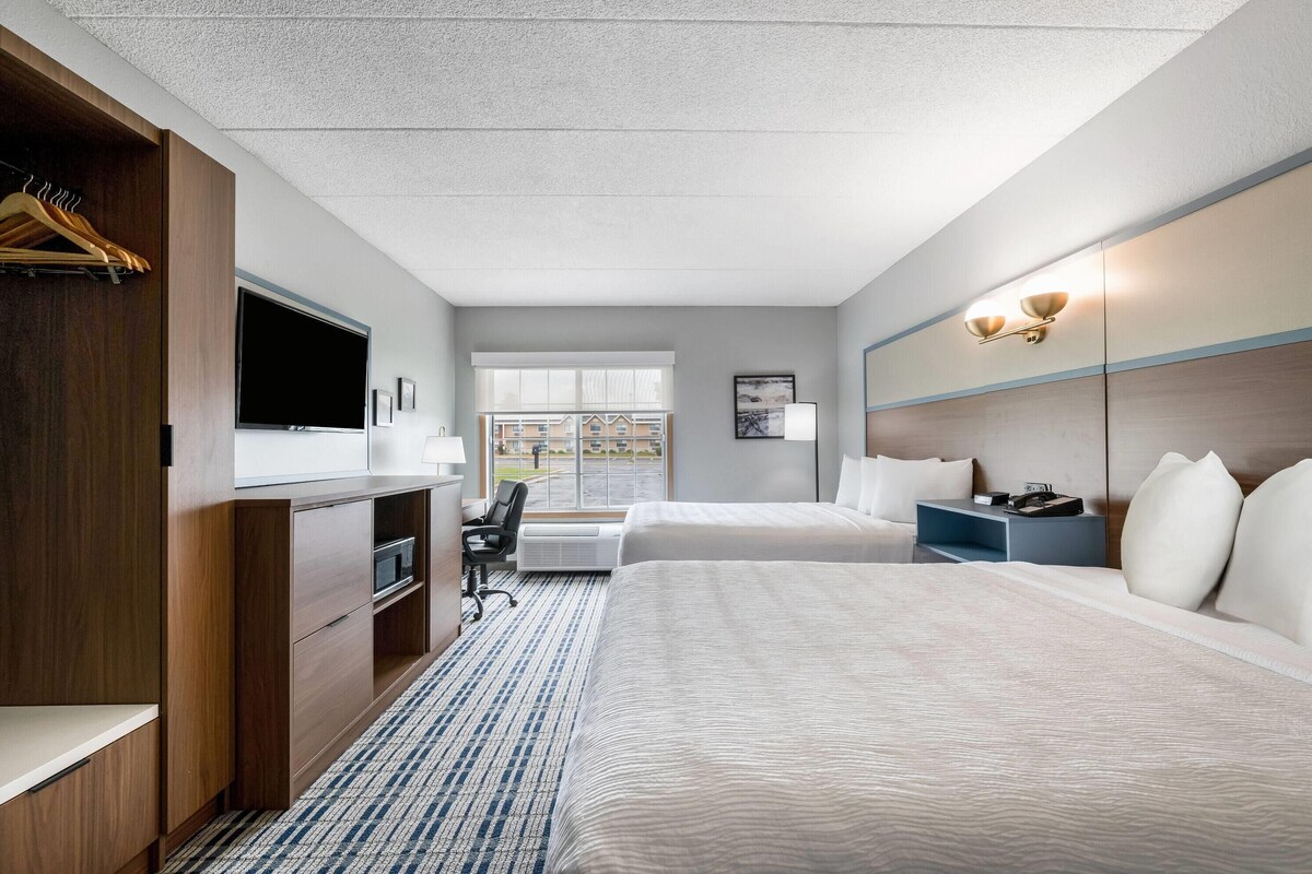 Habitación de hotel con cama, escritorio, silla, televisión y ventana con vistas a edificios.