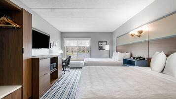 Habitación de hotel con cama, escritorio, silla, televisión y ventana con vistas a edificios.