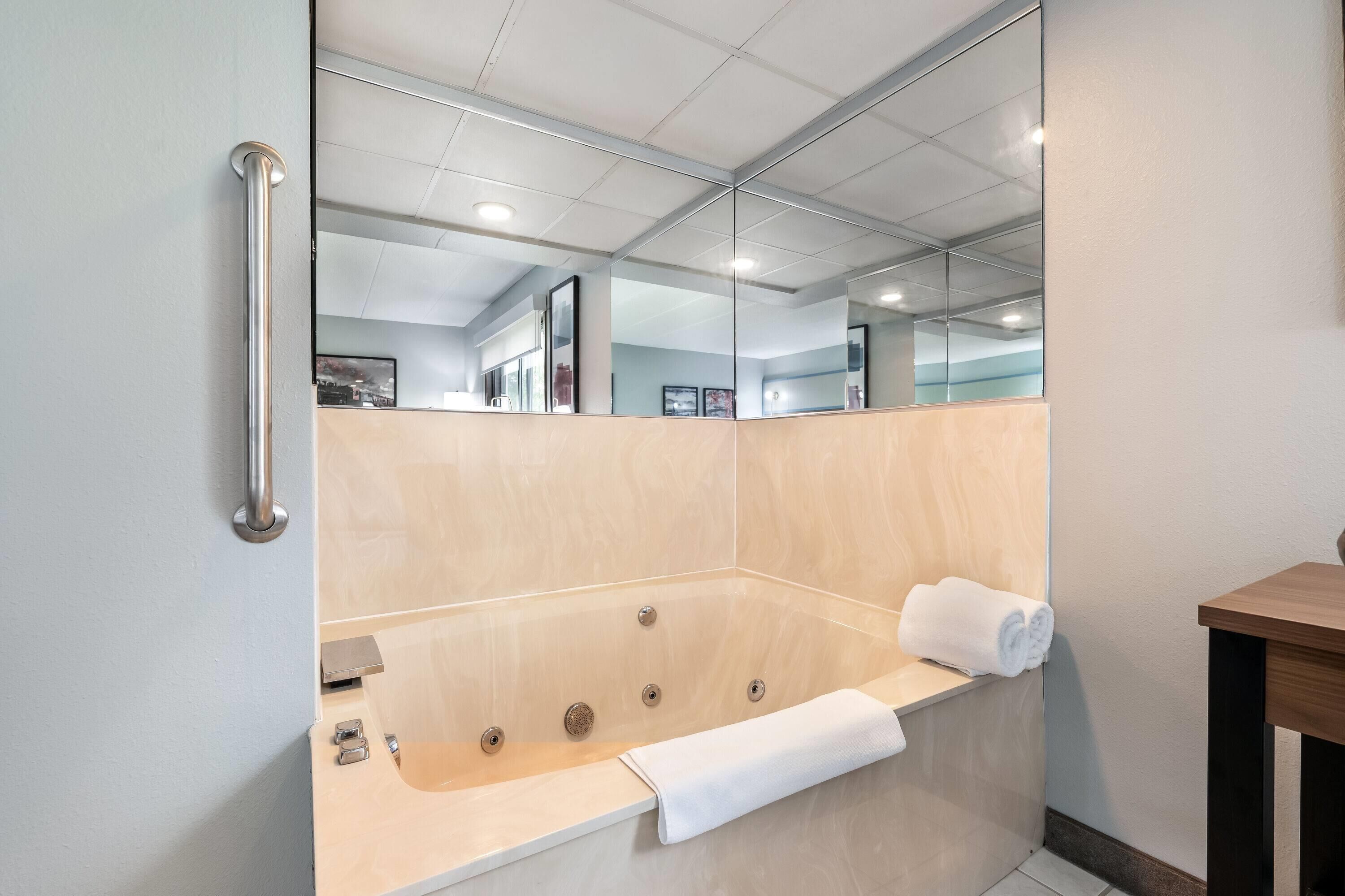 Une salle de bain moderne avec une grande baignoire, une barre d’appui, un banc en bois et un miroir.