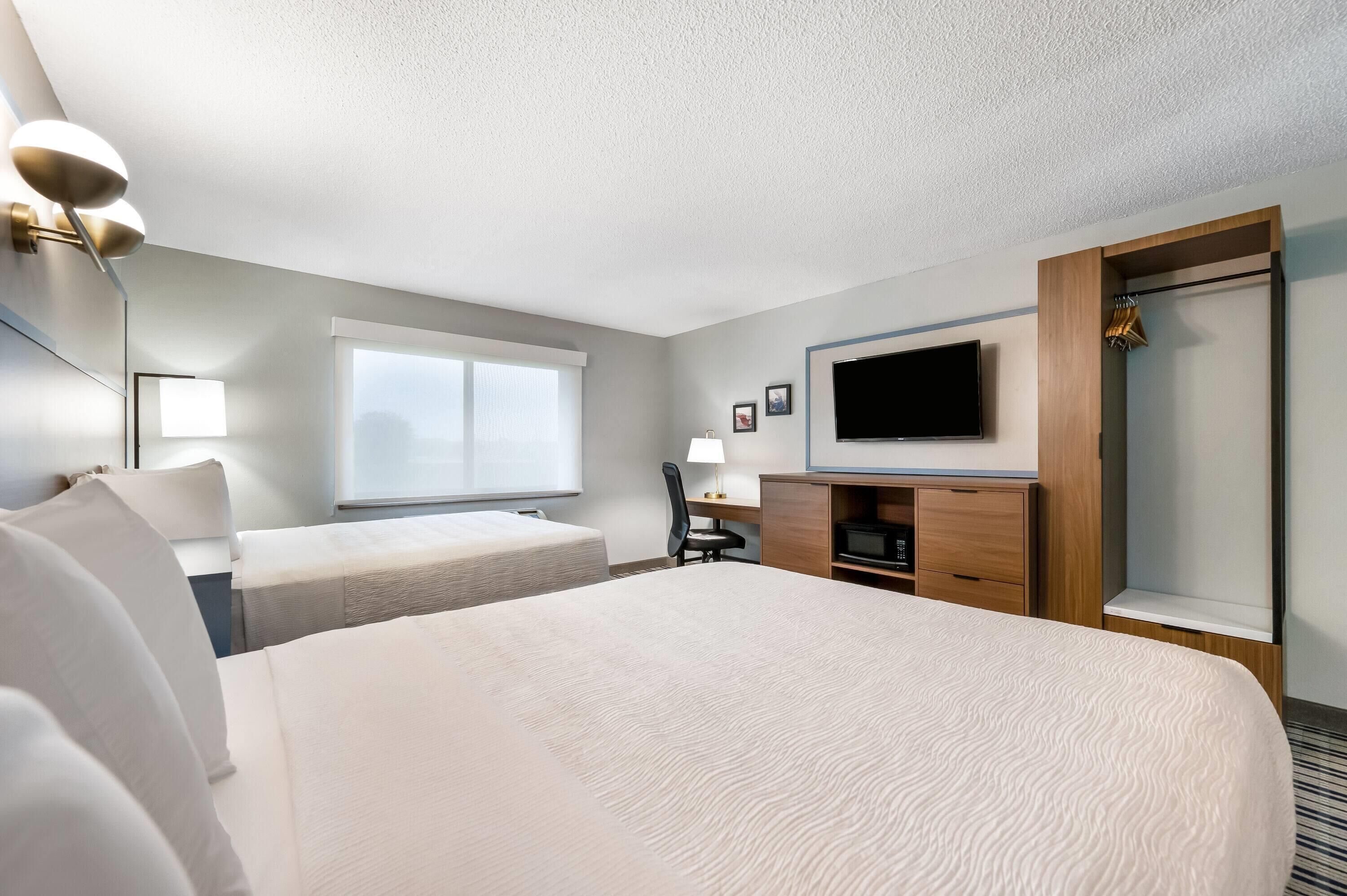 Habitación de hotel con una cama grande, dos camas más pequeñas, un escritorio con silla, un televisor y un armario.