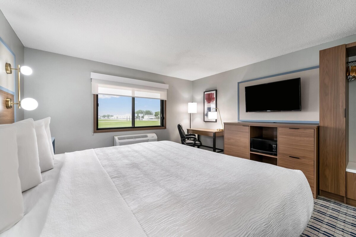 Una habitación de hotel con una cama grande, un escritorio con una silla, un televisor de pantalla plana y una ventana con vistas a un campo de golf.