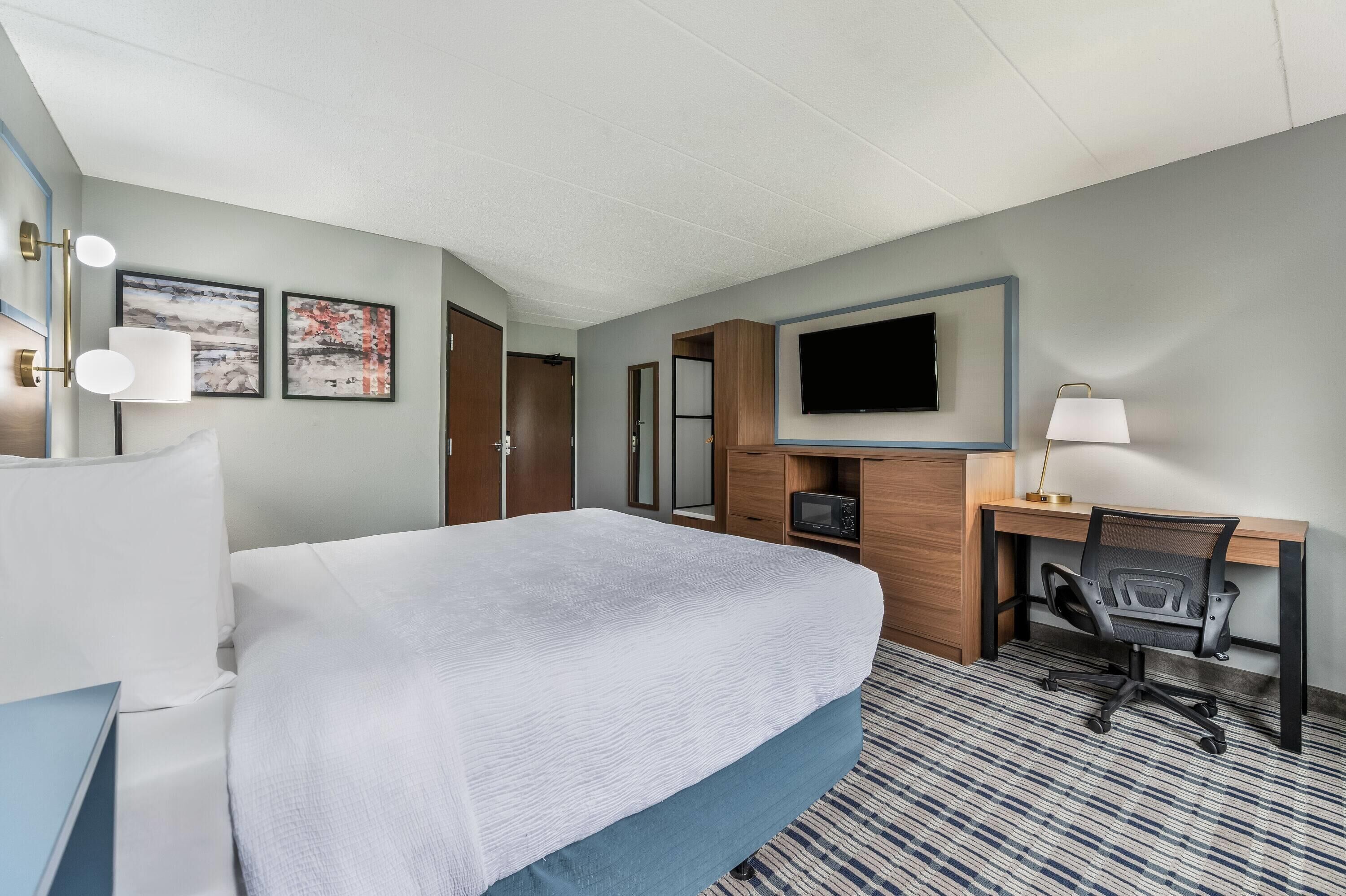A hotel room with a bed, a desk with a chair, a television, and artwork on the wall.