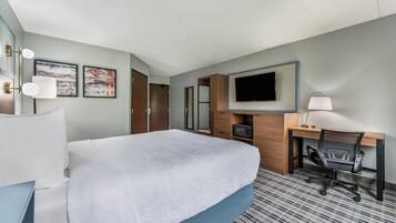 A hotel room with a bed, a desk with a chair, a television, and artwork on the wall.