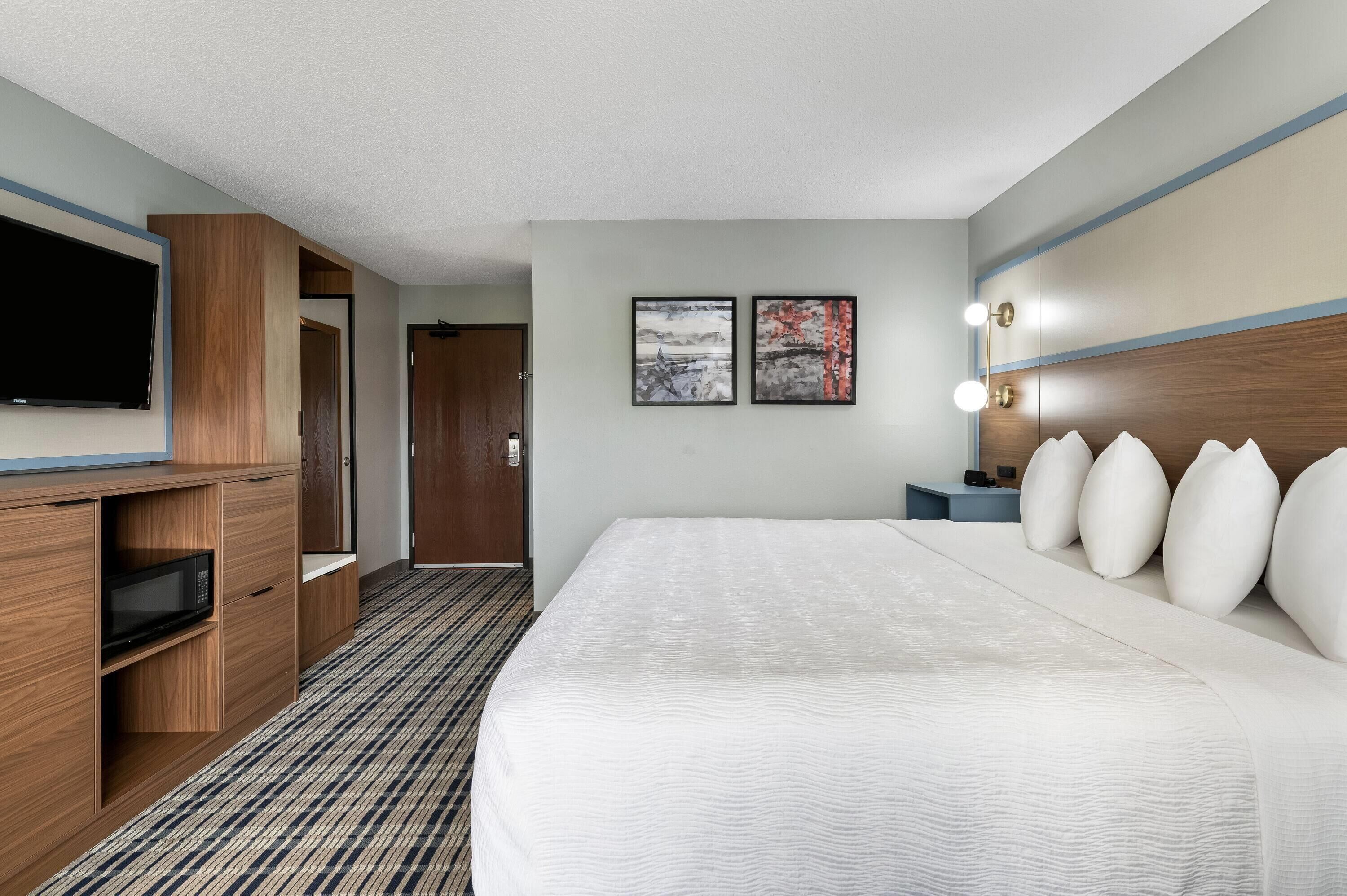 A hotel room with a large bed, a flat-screen TV, a wooden wardrobe, and two framed artworks on the wall.