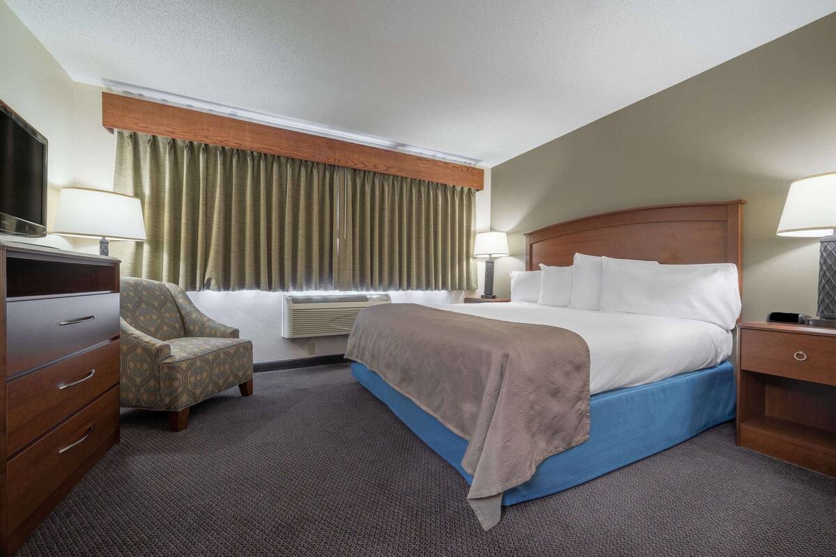 Una habitación de hotel con una cama, una silla, un escritorio y un televisor.