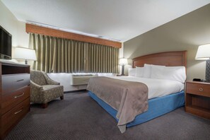 A hotel room with a bed, a chair, a desk, and a TV. - AmericInn by Wyndham Hutchinson (Hutchinson)