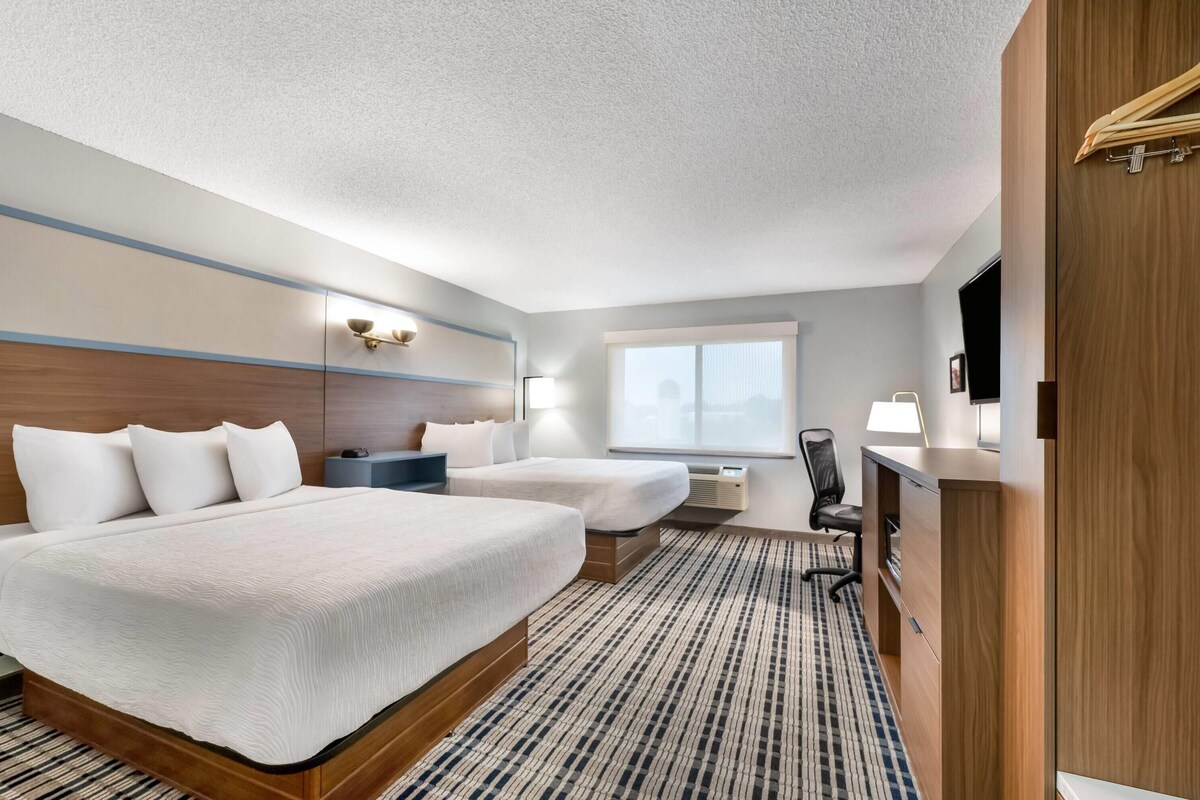 Una habitación de hotel con una cama grande, dos camas más pequeñas, un escritorio, una silla, un televisor y un armario.