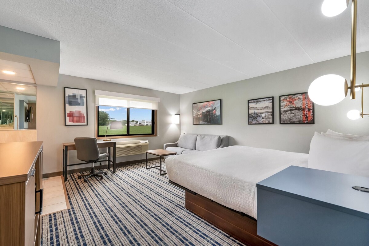 Una habitación de hotel con cama, escritorio, silla y un ventanal grande.
