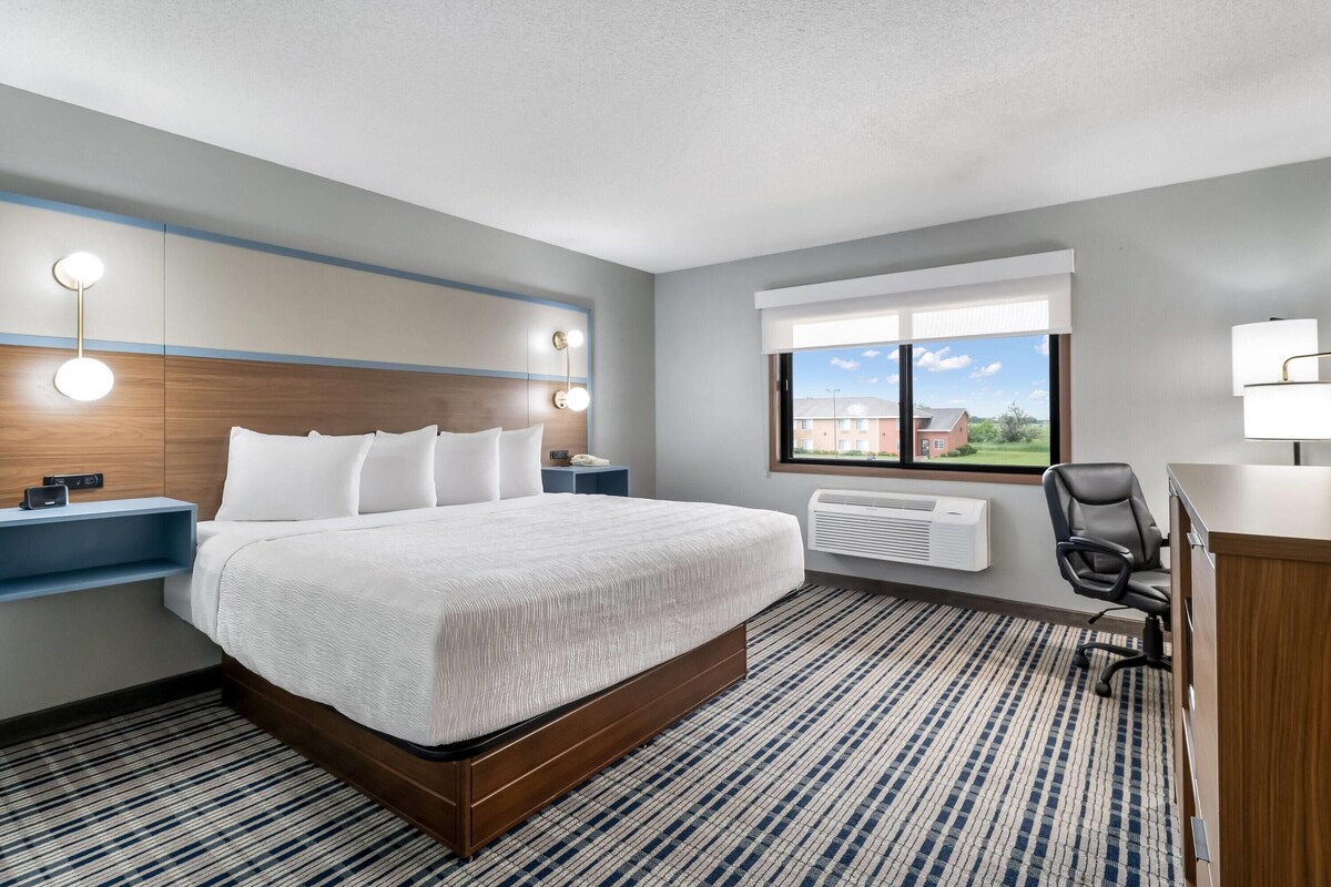 Habitación de hotel con cama, mesitas de noche, escritorio, silla, ventana con vistas y aire acondicionado.
