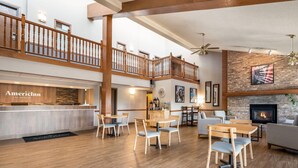 A spacious hotel lobby with a wooden reception desk, multiple seating areas, a fireplace, and a balcony with a wooden railing. - AmericInn by Wyndham Hutchinson (Hutchinson)