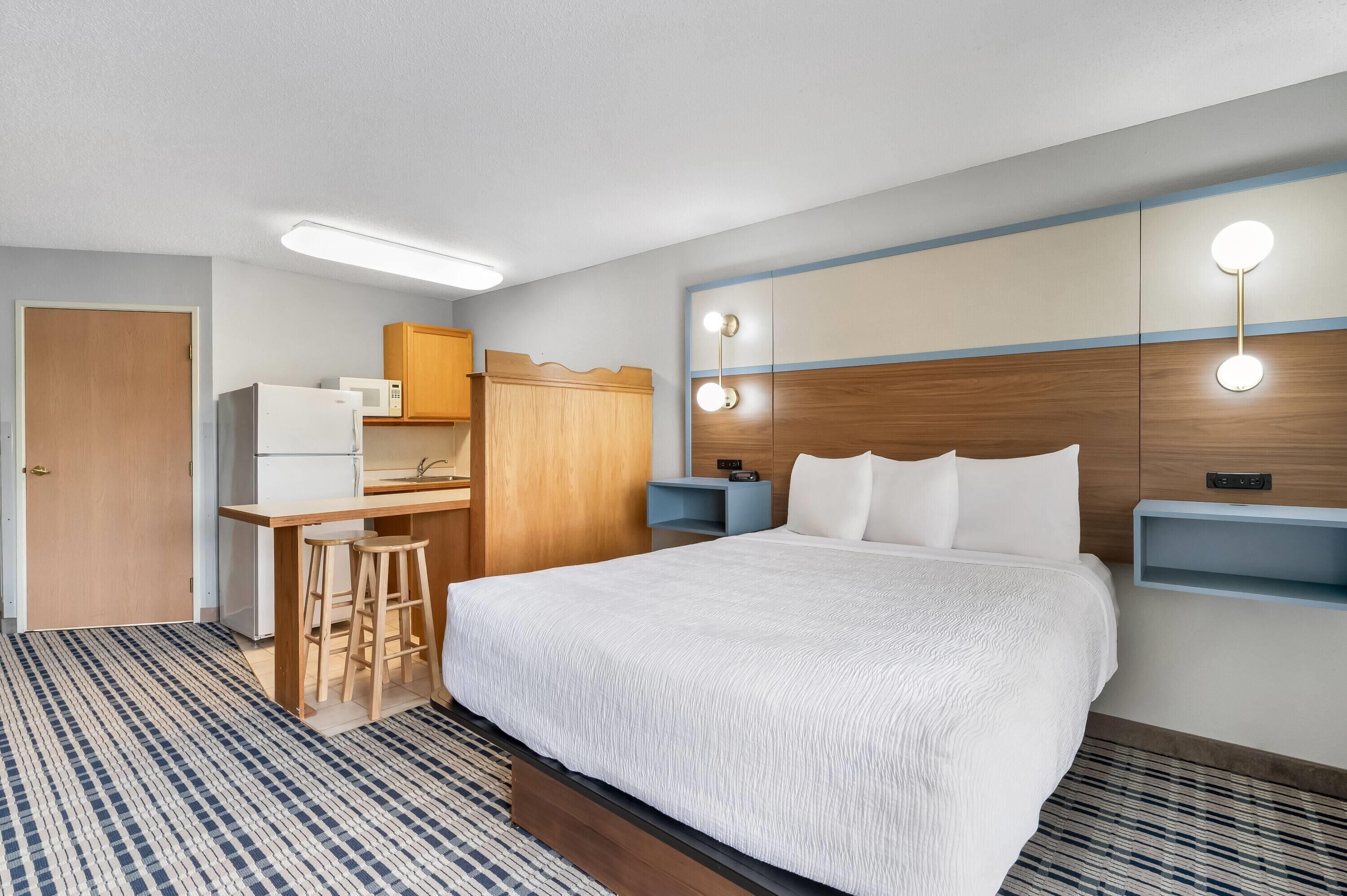 A hotel room with a bed, a desk with a microwave, a wardrobe, and bedside lamps.